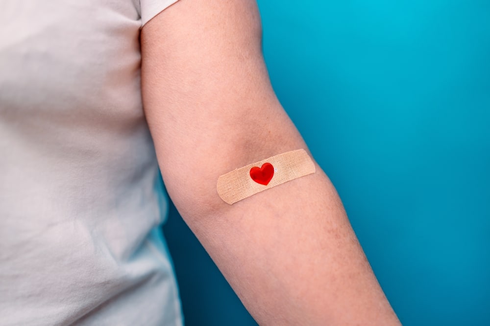 Une femme avec un bandage sur le bras, symbolisé par un cœur rouge.
