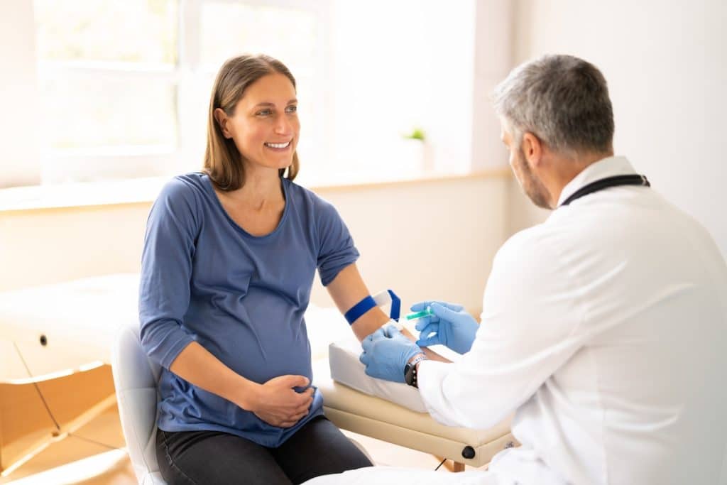 Femme enceinte souriante lors d'une consultation pendant qu'un professionnel de la santé se prépare à prélever du sang pour un rapport SEO généré automatiquement.